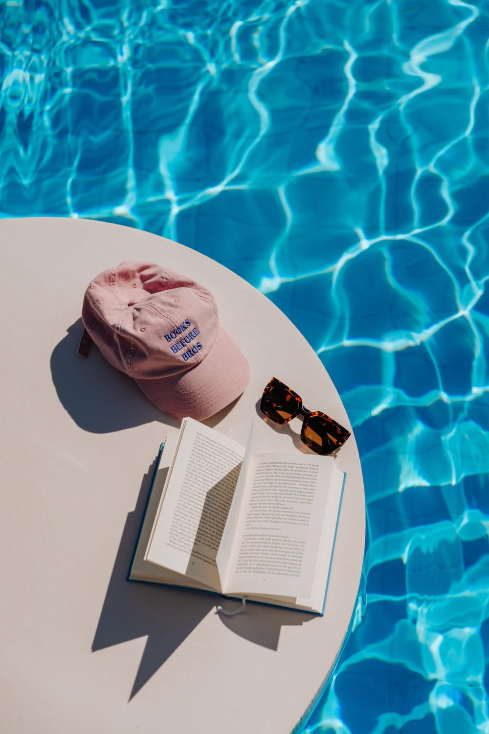 Bücher, Cap und Sonnenbrille am Beckenrand